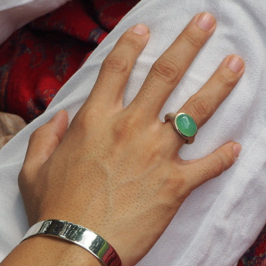 A hand wearing a silver ring with a large green chrysoprase cabochon gemstone.